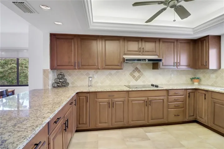 Kitchen featuring under cabinet range hood, black electric cooktop, a raised ceiling, light stone countertops, and recessed lighting