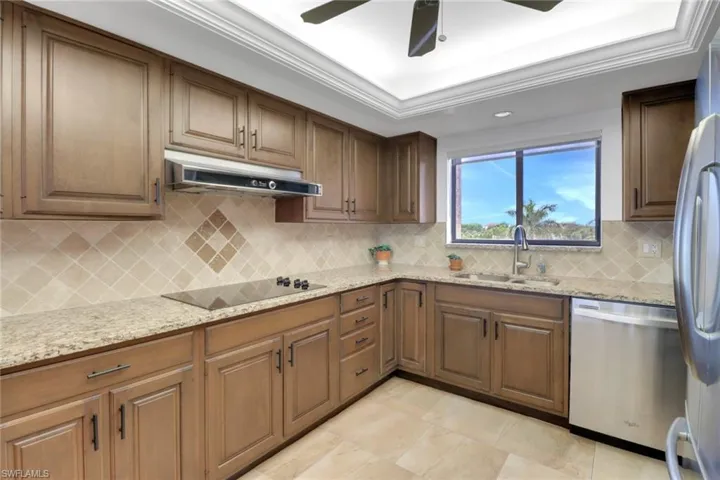 Kitchen with stainless steel appliances, a sink, under cabinet range hood, light stone countertops, and tasteful backsplash