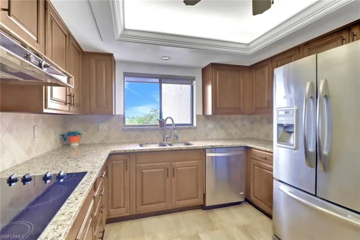Kitchen with appliances with stainless steel finishes, a sink, under cabinet range hood, decorative backsplash, and brown cabinetry