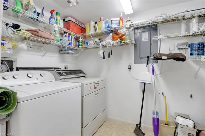 Laundry room with washer and clothes dryer, electric panel, light tile patterned floors, and baseboards