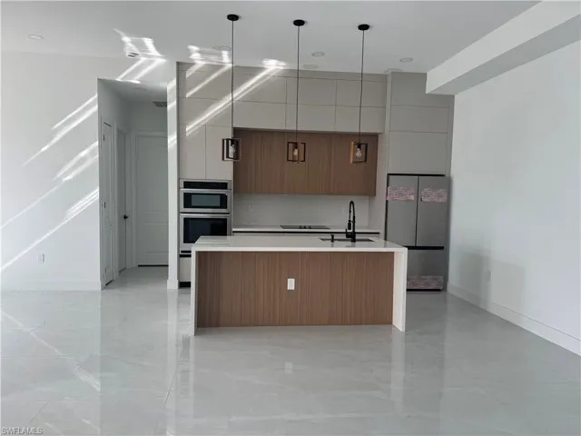 Kitchen with modern cabinets, brown cabinetry, appliances with stainless steel finishes, a kitchen island with sink, and light stone counters