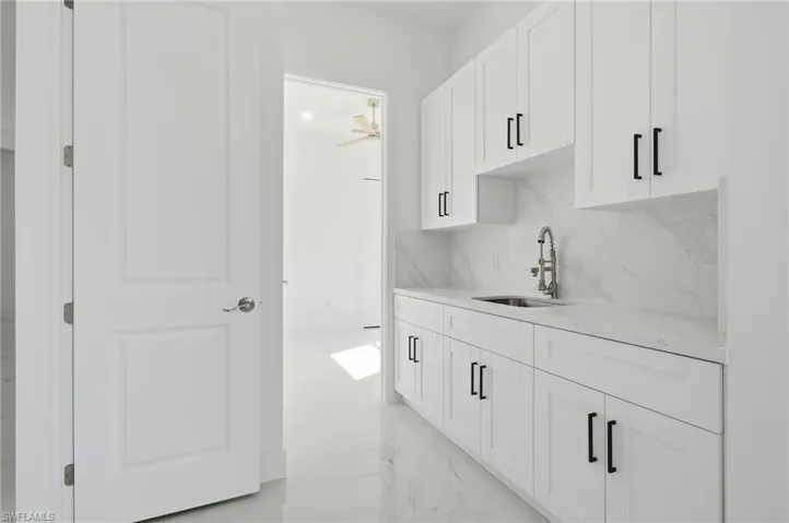 Bar featuring white cabinets, light stone counters, light marble finish flooring, and tasteful backsplash