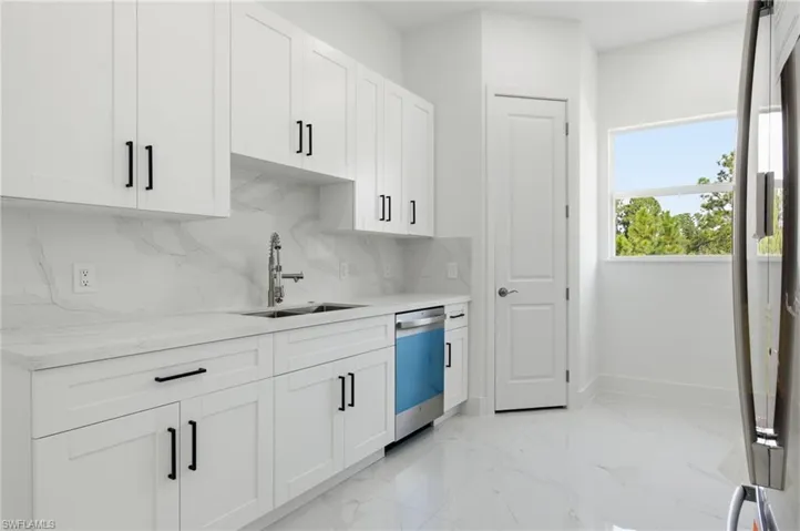 Kitchen featuring white cabinetry, tasteful backsplash, light marble finish floors, appliances with stainless steel finishes, and light stone counters