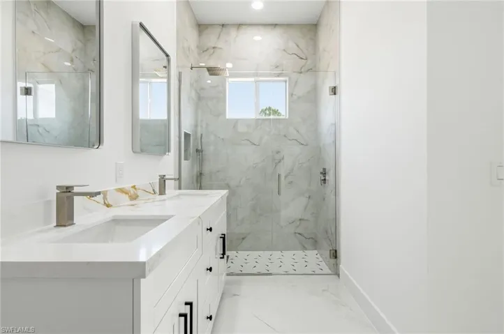Bathroom with light marble finish floors, double vanity, and a marble finish shower