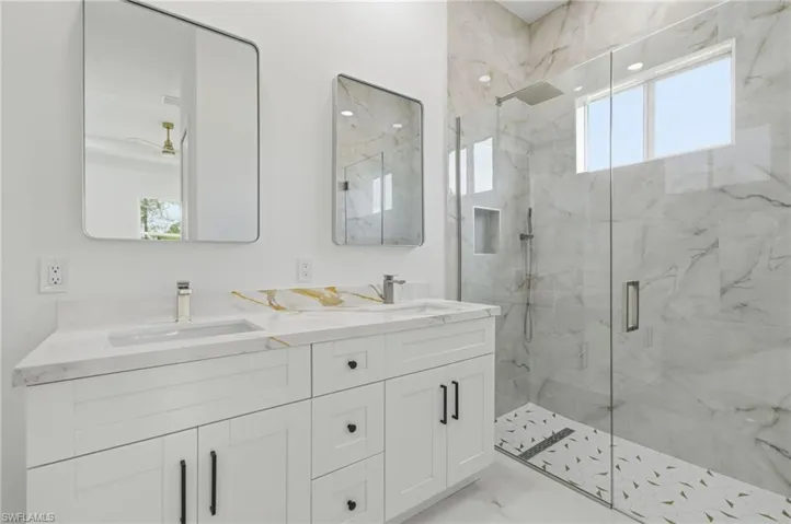 Bathroom with double vanity, a marble finish shower, and light marble finish floors