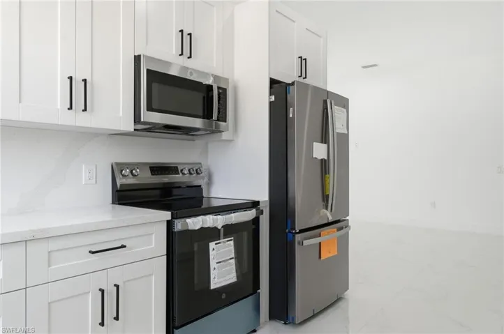 Kitchen featuring appliances with stainless steel finishes, white cabinetry, light marble finish flooring, light stone counters, and tasteful backsplash