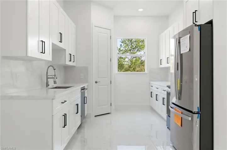 Kitchen featuring appliances with stainless steel finishes, light stone countertops, decorative backsplash, white cabinetry, and light marble finish floors