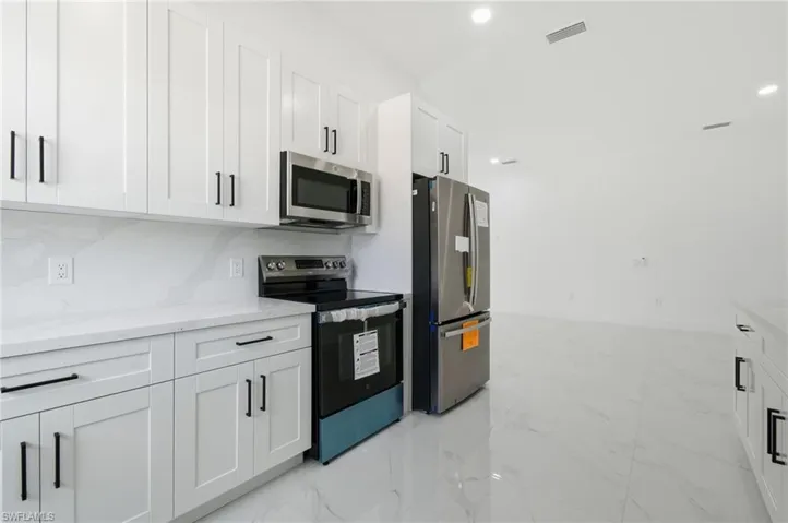 Kitchen featuring stainless steel appliances, white cabinetry, light marble finish flooring, recessed lighting, and light stone counters