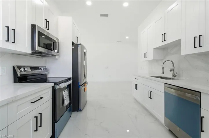 Kitchen featuring stainless steel appliances, light stone counters, white cabinetry, recessed lighting, and backsplash