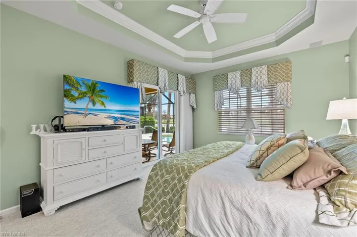 Bedroom featuring ceiling fan, access to exterior, a raised ceiling, crown molding, and light colored carpet