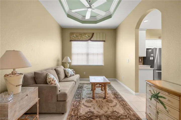 Living room featuring light tile patterned floors, ceiling fan, a raised ceiling, and ornamental molding