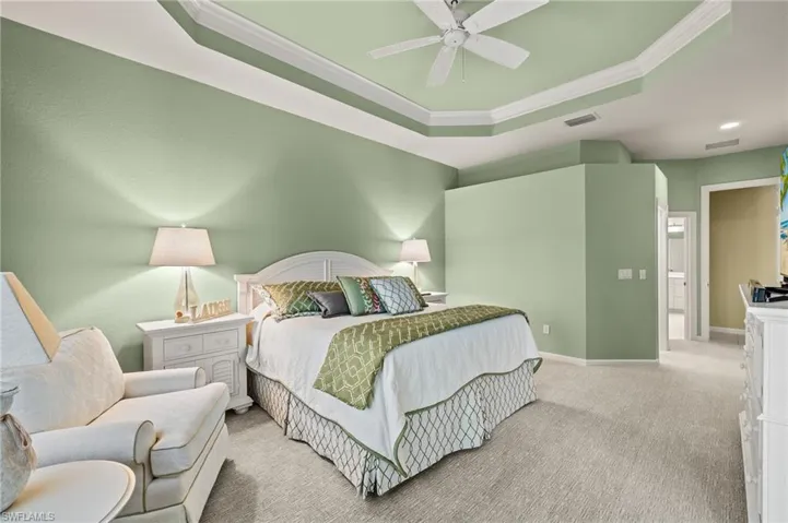 Carpeted bedroom featuring ornamental molding, ceiling fan, and a raised ceiling