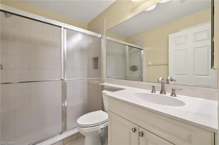Bathroom with toilet, vanity, tile patterned flooring, and a shower with shower door
