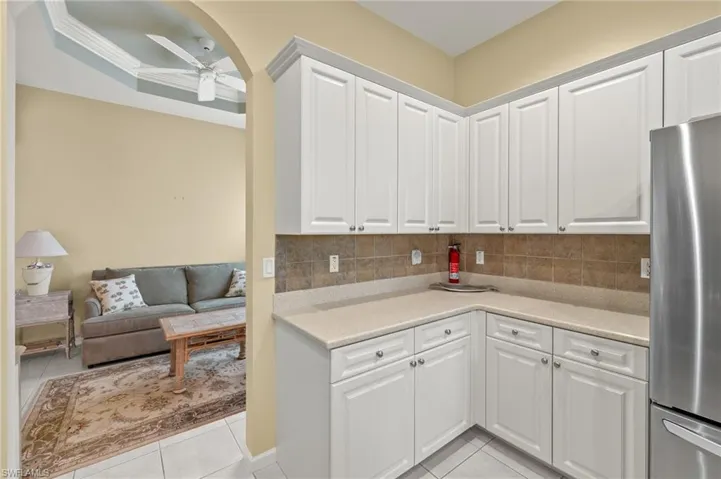 Kitchen featuring ornamental molding, tasteful backsplash, ceiling fan, white cabinets, and stainless steel fridge
