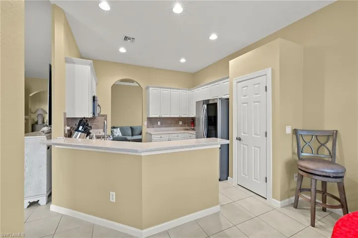 Kitchen featuring a kitchen bar, stainless steel appliances, kitchen peninsula, decorative backsplash, and white cabinetry