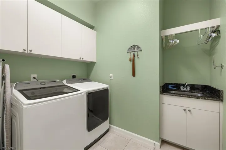 Clothes washing area with washer and clothes dryer, cabinets, sink, and light tile patterned floors