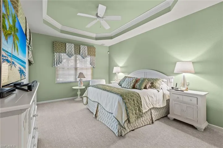 Carpeted bedroom featuring ornamental molding, ceiling fan, and a tray ceiling