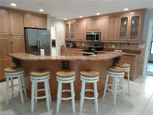 Kitchen with glass insert cabinets, stainless steel appliances, recessed lighting, light stone counters, and light tile patterned floors