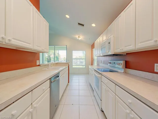 Kitchen with white cabinets, vaulted ceiling, white appliances, and sink