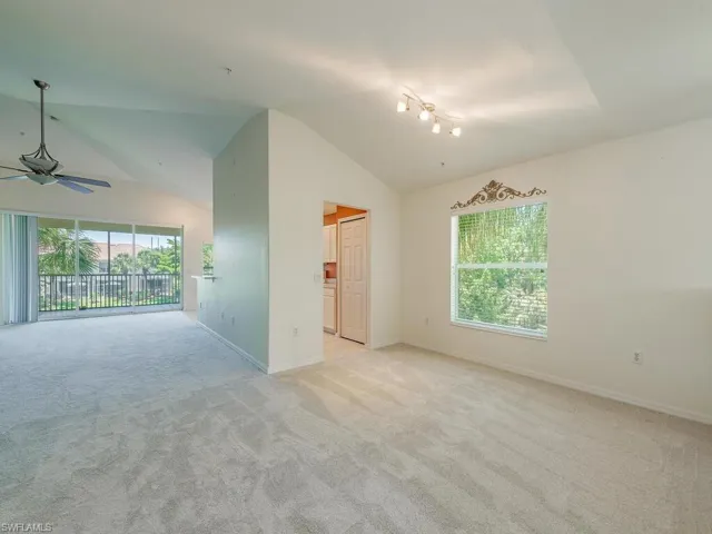 Unfurnished living room featuring light carpet, a wealth of natural light, ceiling fan, and vaulted ceiling