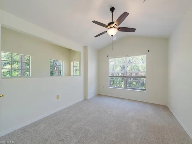 Empty room featuring carpet floors, ceiling fan, and vaulted ceiling