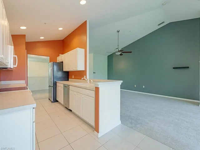 Kitchen with lofted ceiling, light tile patterned floors, ceiling fan, stainless steel appliances, and sink