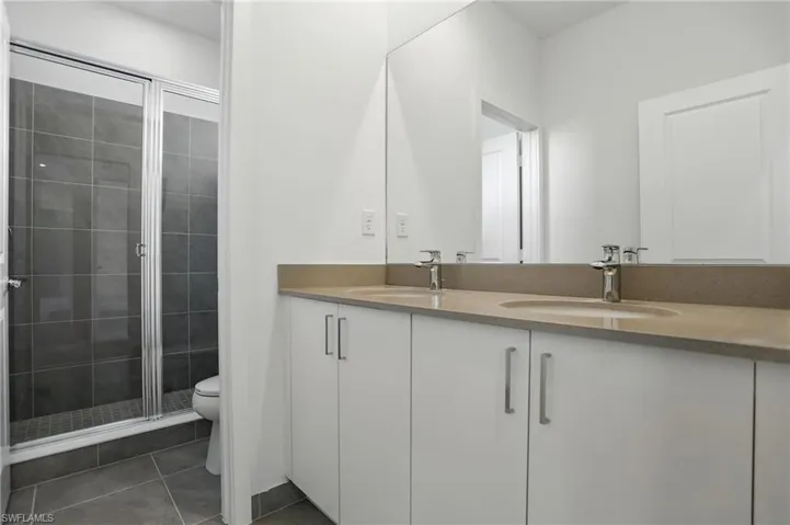 Full bathroom featuring double vanity, dark tile patterned flooring, and a stall shower