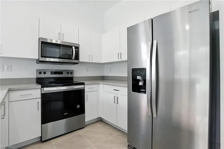 Kitchen with stainless steel appliances, white cabinetry, light countertops, and light tile patterned flooring