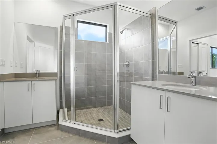Bathroom with a stall shower, two vanities, and light tile patterned floors