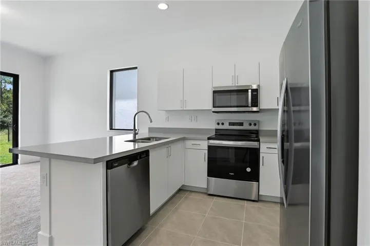 Kitchen with appliances with stainless steel finishes, a peninsula, light tile patterned floors, white cabinets, and recessed lighting