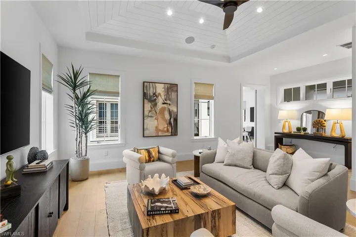 Living room featuring a raised ceiling, light wood-style floors, a ceiling fan, recessed lighting, and baseboards