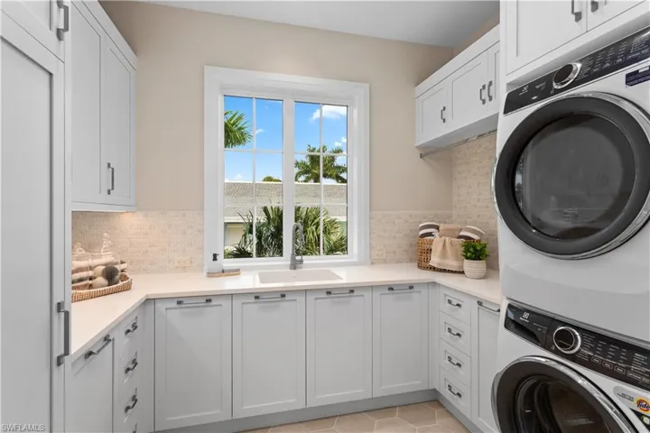 Laundry area featuring stacked washing machine and dryer, cabinet space, and light tile patterned floors