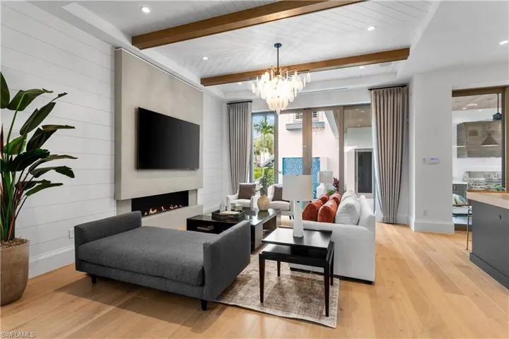 Living area featuring beamed ceiling, light wood-style flooring, a chandelier, a lit fireplace, and recessed lighting