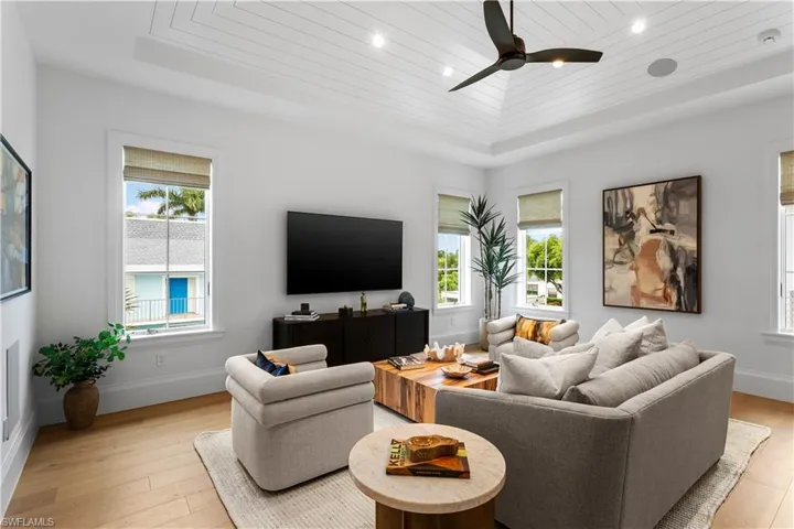 Living room featuring a raised ceiling, light wood-style floors, a ceiling fan, baseboards, and wooden ceiling