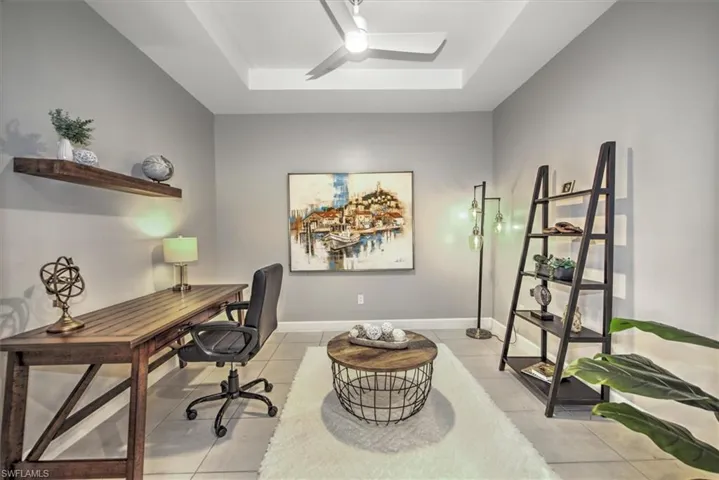 Office area with light tile patterned floors, baseboards, a tray ceiling, and a ceiling fan