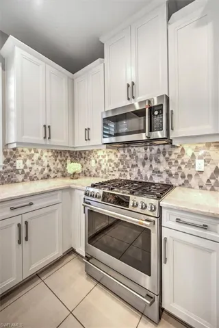 Kitchen featuring backsplash, white cabinetry, stainless steel appliances, light tile patterned flooring, and light stone countertops