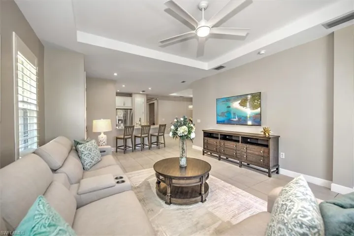 Living room with light tile patterned floors, a tray ceiling, baseboards, and a ceiling fan