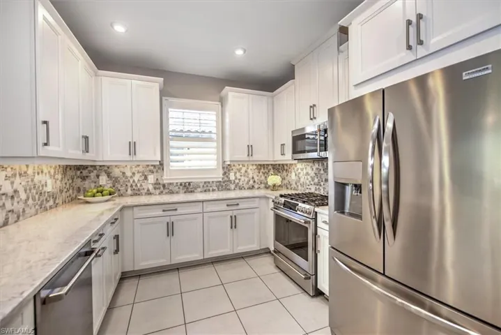 Kitchen featuring light stone countertops, light tile patterned floors, decorative backsplash, appliances with stainless steel finishes, and white cabinetry