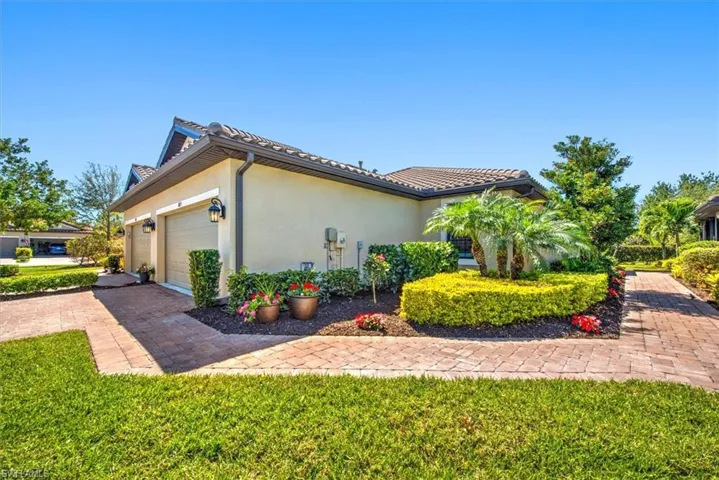 View of side of villa with stucco siding, decorative driveway, an attached garage, and a tiled roof