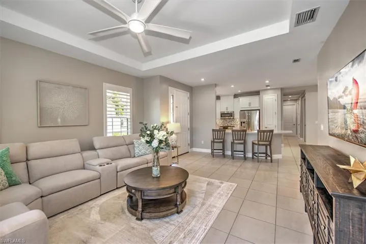 Living area featuring visible vents, baseboards, light tile patterned flooring, a raised ceiling, and a ceiling fan