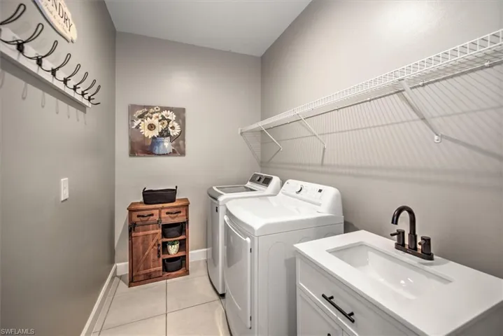 Laundry room with light tile patterned floors, baseboards, cabinet space, a sink, and washing machine and dryer