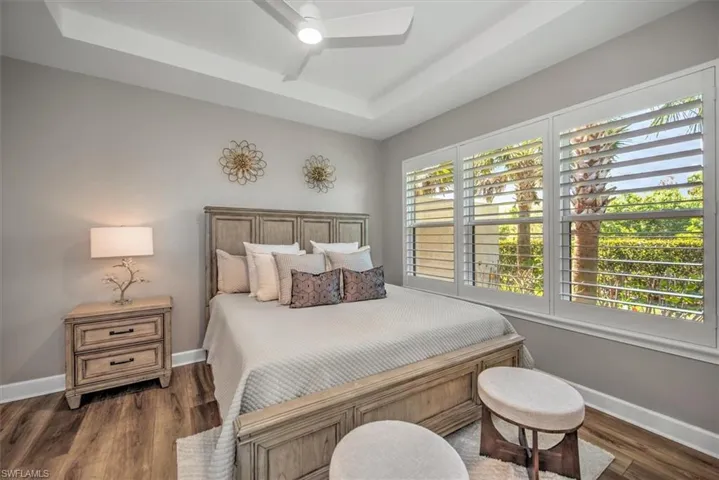 Bedroom with a tray ceiling, multiple windows, wood finished floors, and baseboards