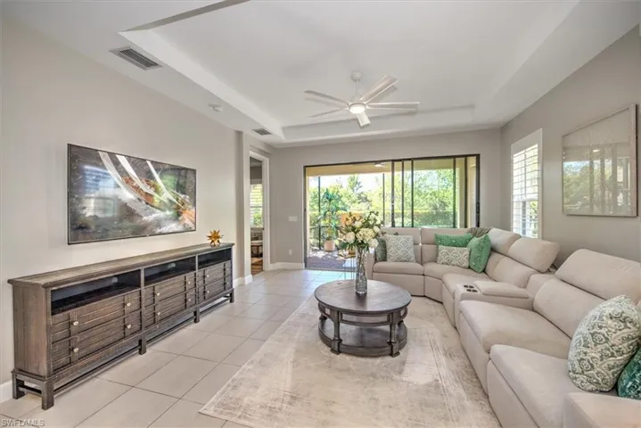 Living room featuring ceiling fan, visible vents, a raised ceiling, and light tile patterned flooring