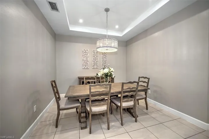 Dining room with a tray ceiling, baseboards, a notable chandelier, and visible vents