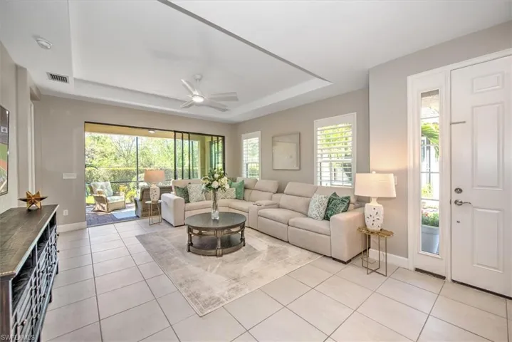 Living room featuring a ceiling fan, visible vents, baseboards, a tray ceiling, and light tile patterned flooring