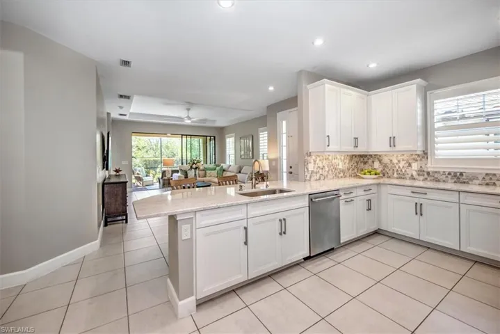 Kitchen with a sink, stainless steel dishwasher, open floor plan, a peninsula, and light tile patterned floors