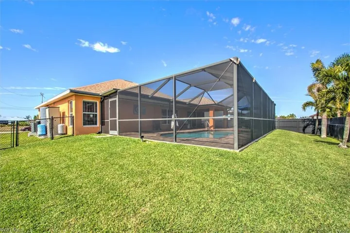 Rear view of house with a fenced in pool, glass enclosure, and a lawn
