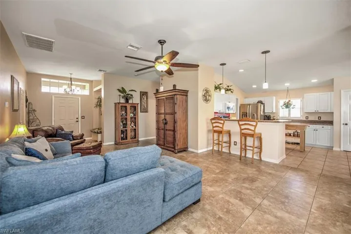 Tiled living room featuring ceiling fan with notable chandelier and vaulted ceiling