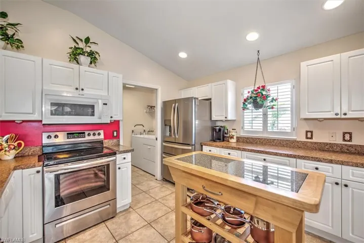 Kitchen with stainless steel appliances, washing machine and clothes dryer, white cabinets, vaulted ceiling, and light tile patterned flooring