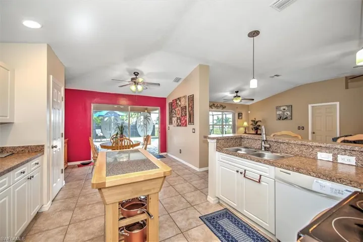 Kitchen featuring lofted ceiling, sink, white cabinetry, decorative light fixtures, and light tile patterned floors